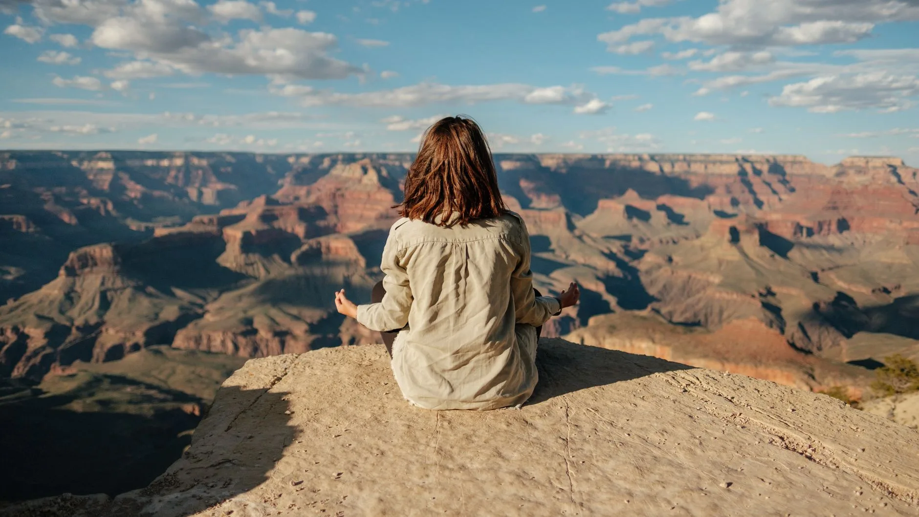 A woman meditating cross-legged with red rock cliffs behind her